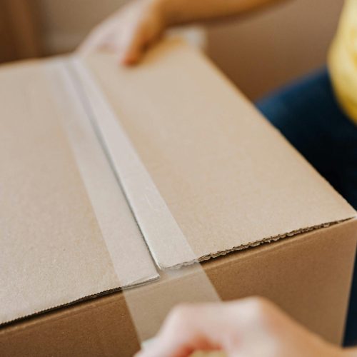 Close-up of a person sealing a cardboard box with tape, suggesting relocation or delivery.